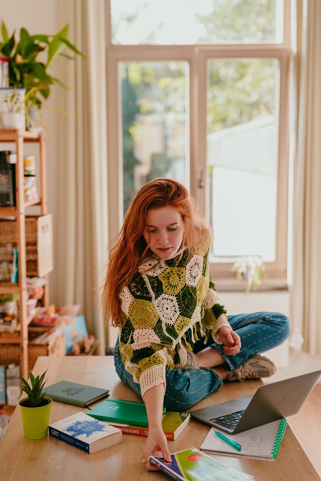 Yasmine, the founder of Learn Dutch with Yas, sitting on a desk while organizing Dutch vocabulary and grammar books