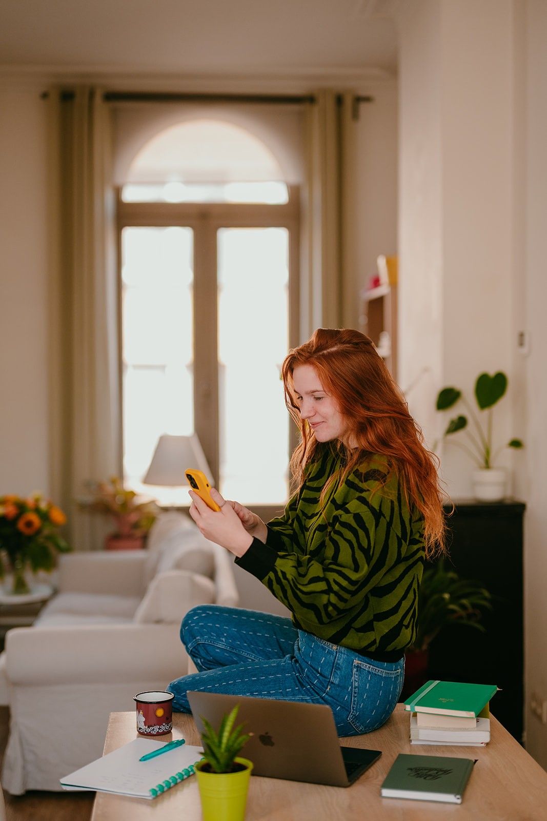 Yasmine, the founder of Learn Dutch with Yas, sitting on a desk while smiling at her smartphone