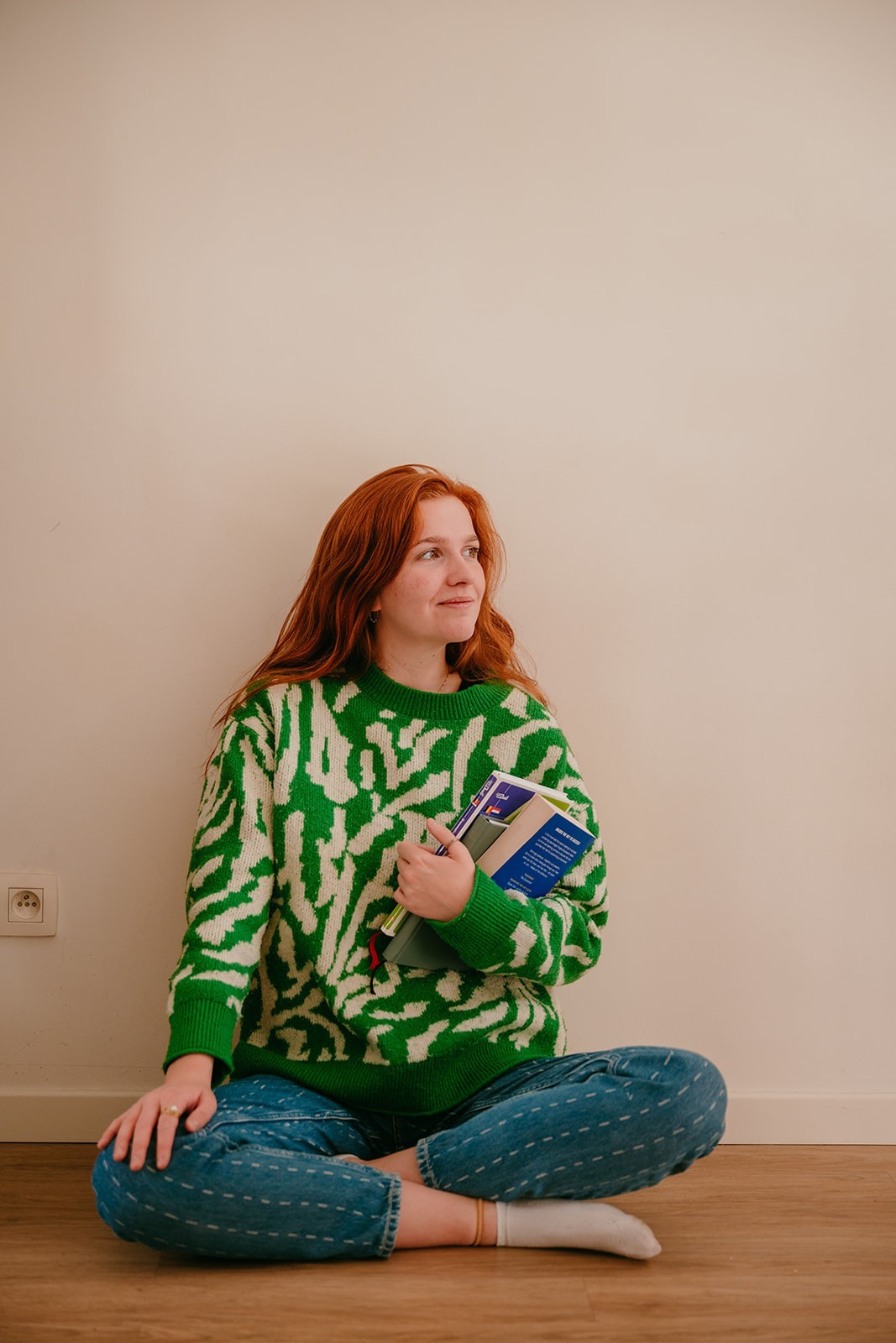 Yasmine, the founder of Learn Dutch with Yas, sitting on the floor while holding Dutch vocabulary books