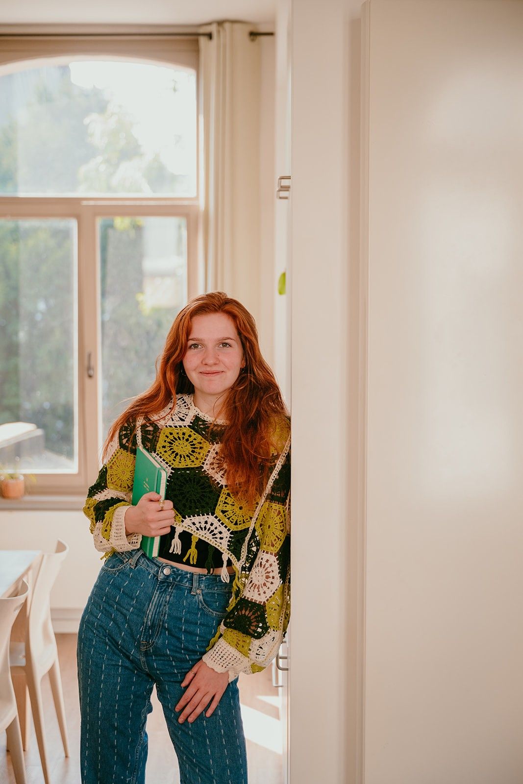 Yasmine, the founder of Learn Dutch with Yas, leaning against a door opening and holding a Dutch vocabulary book